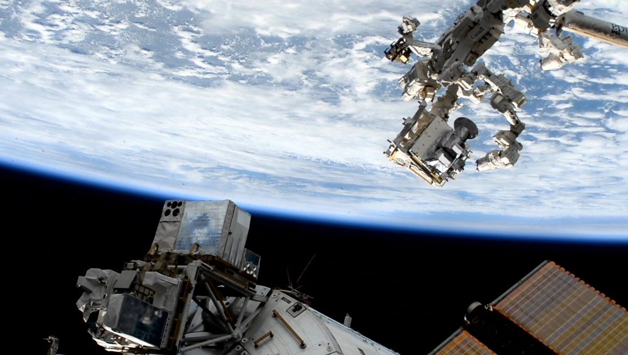 View from space showing the International Space Station with Earth in the background. The station's robotic arm and solar panels are visible, with Earth’s blue and white surface creating a vibrant backdrop.